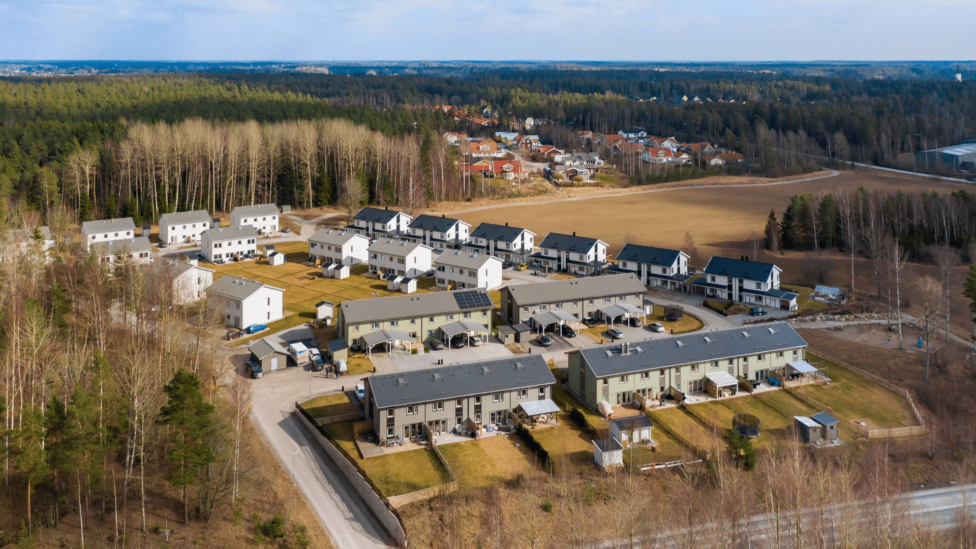 Flygbild över radhusområde med gröna gårdar och parkerade bilar.