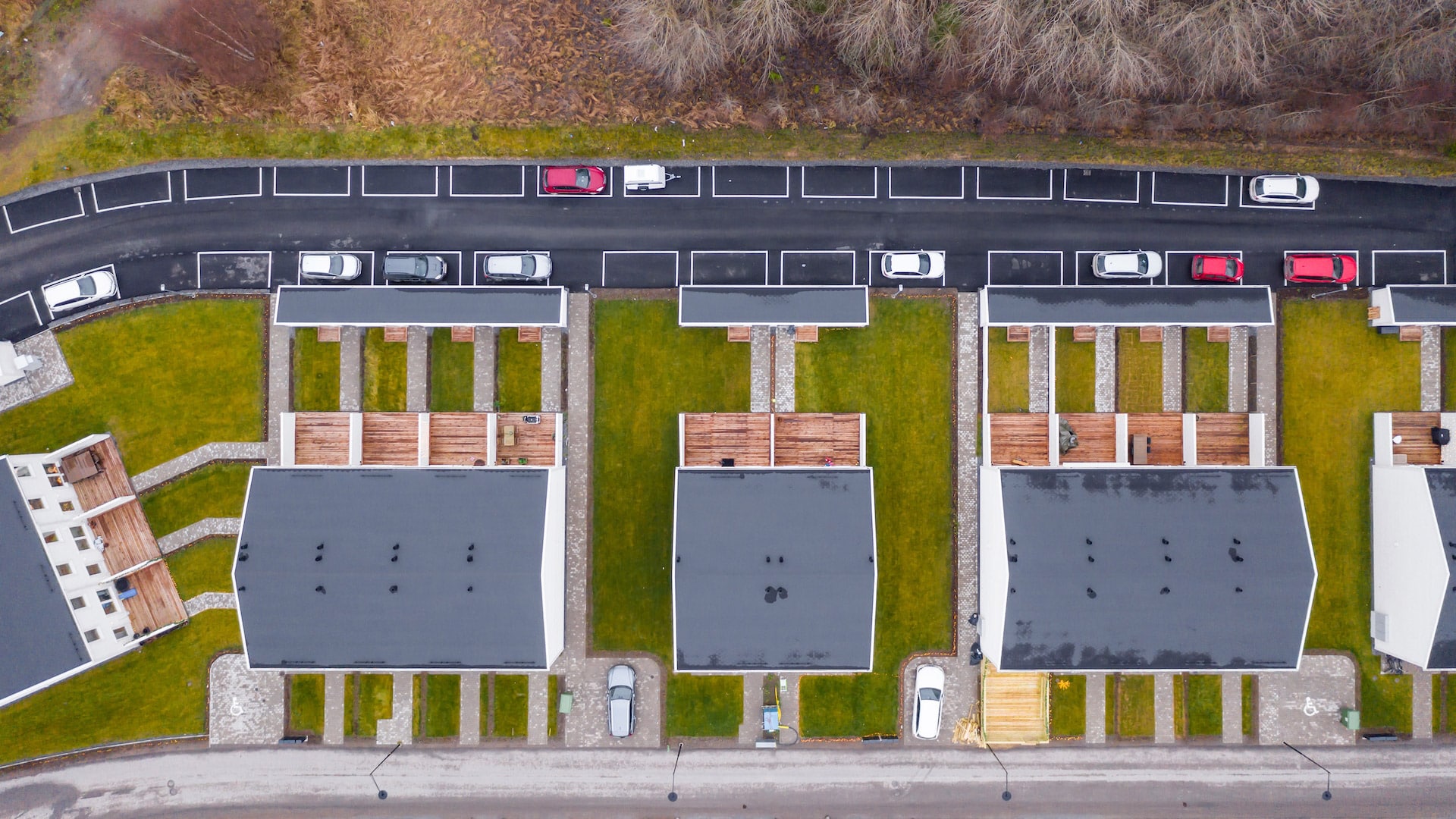 Flygbild över radhusområde med gröna gårdar och parkerade bilar.